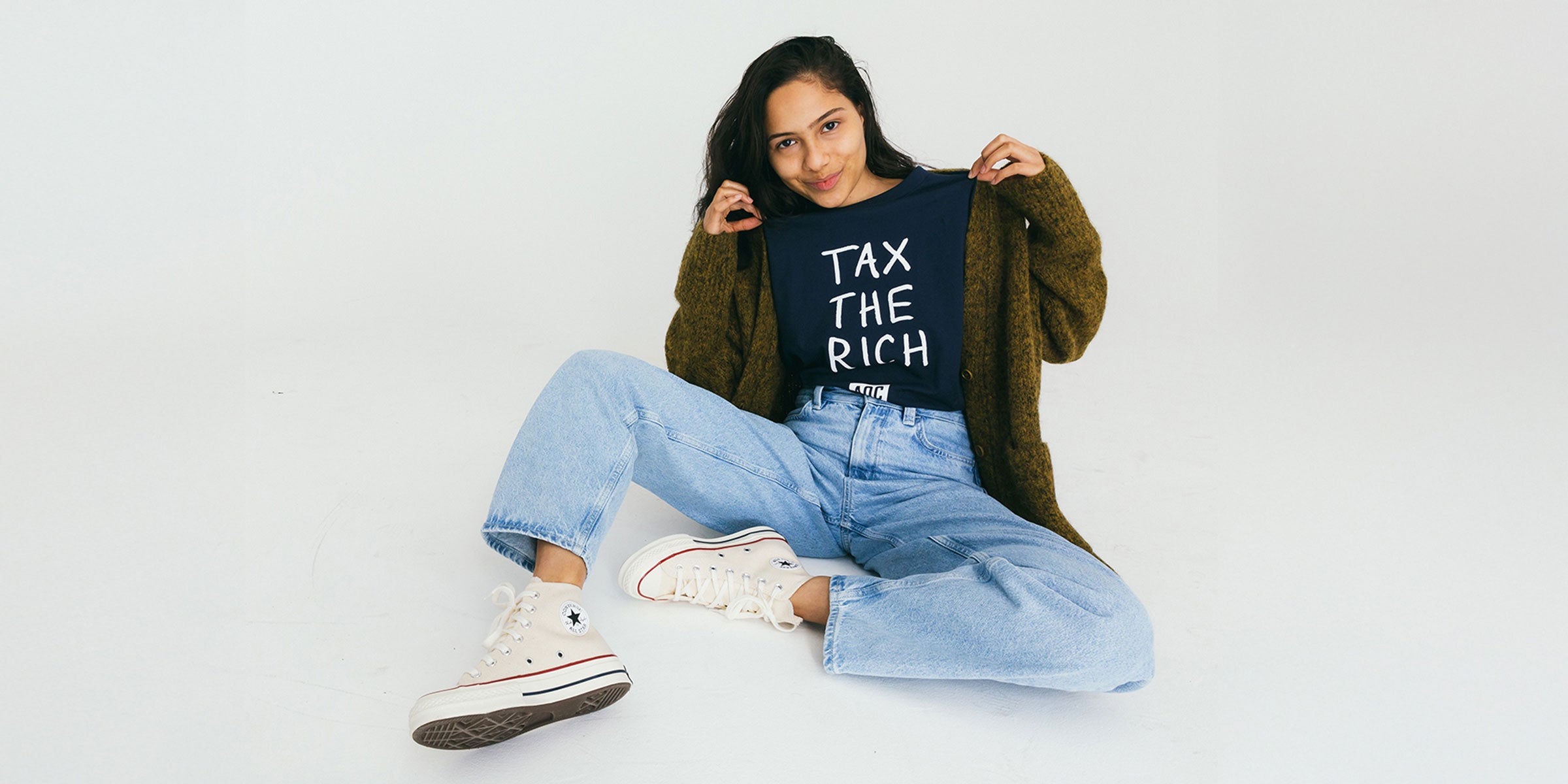 Person wearing a t-shirt with 'Tax the Rich' text on a plain background
